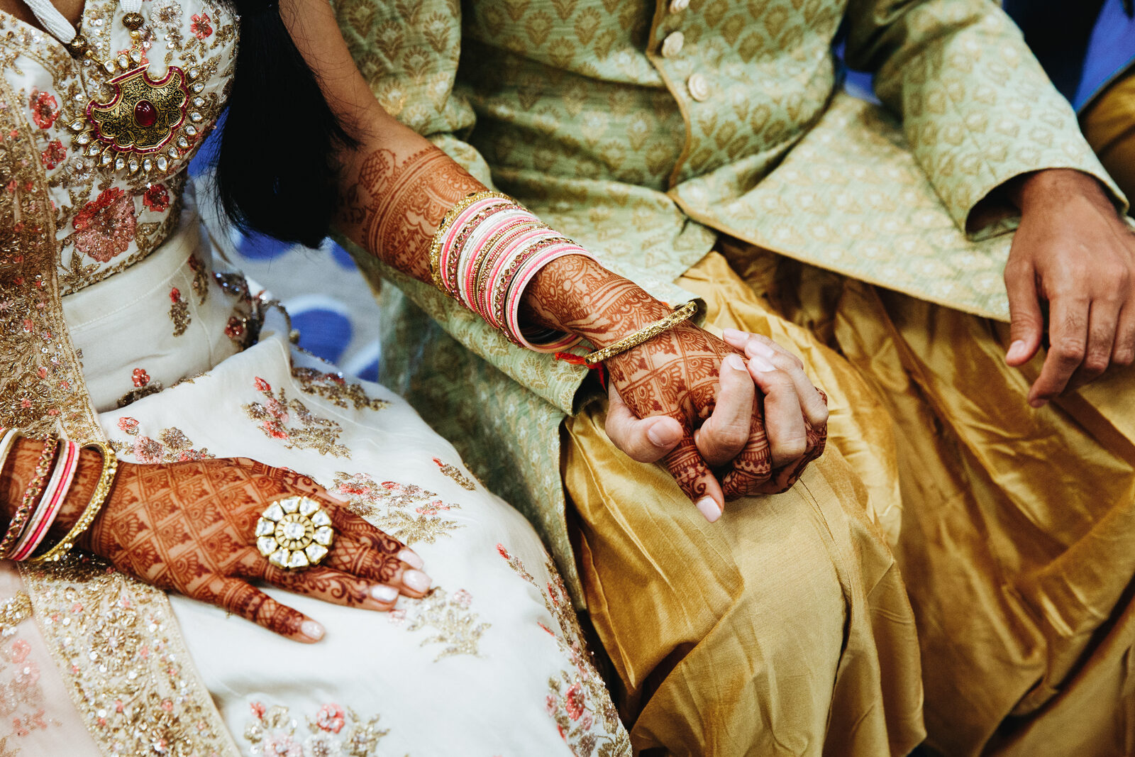 An Indian bride and groom holding hands at their wedding, mehndi on her hands